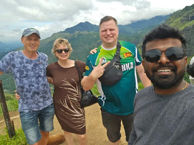 Three guests and Dhanuka smiling together on a green hillside in the hill country